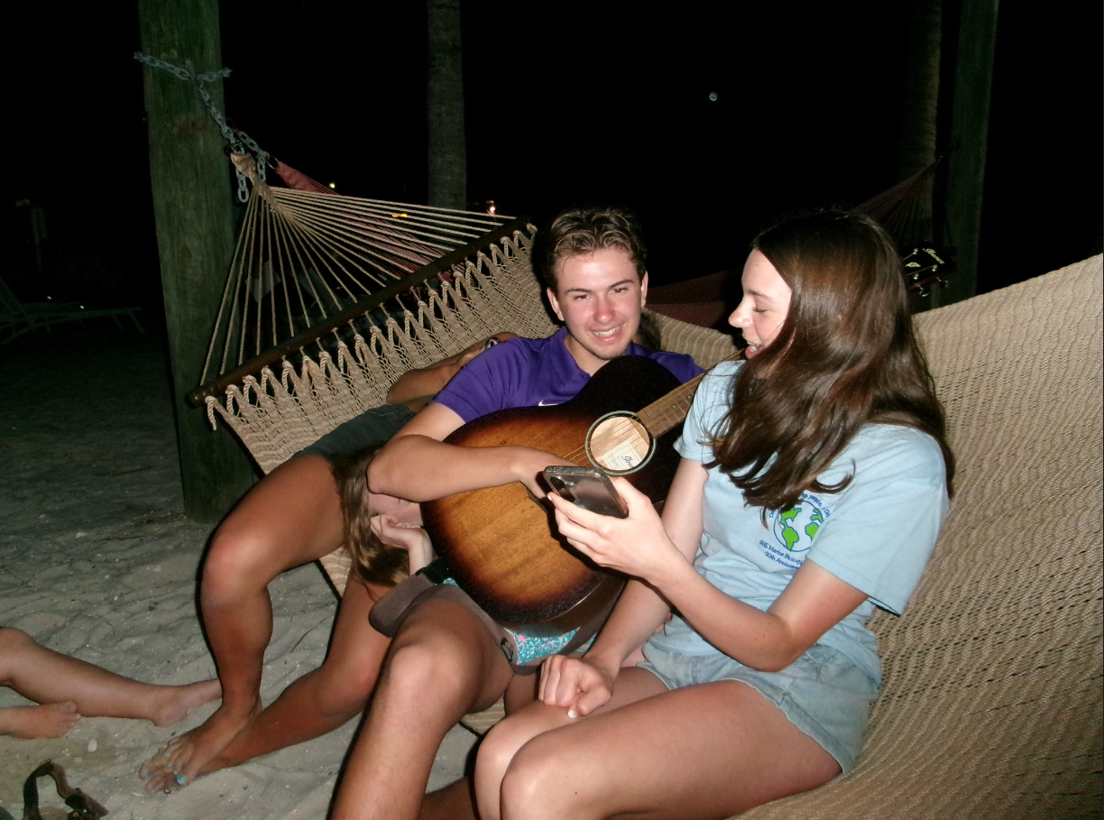 Isaac playing guitar and singing with friends in a hammock in the Florida Keys.
